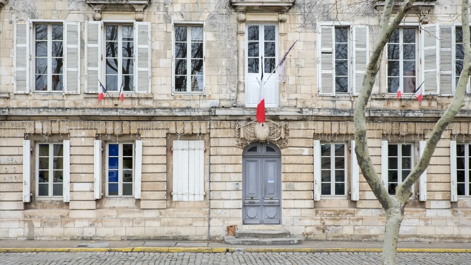 Façade en pierre claire d’une mairie, drapeau français au balcon