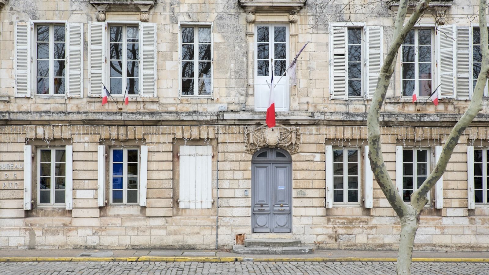 Façade en pierre claire d’une mairie, drapeau français au balcon